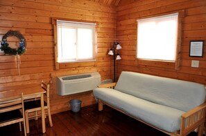 Een chalet met houten inrichting, een bank, een tafel, stoelen en een wandairconditioner.