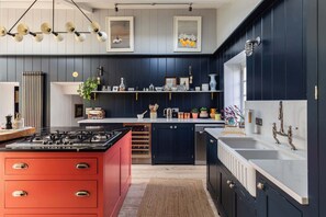 A modern kitchen with dark cabinetry, a red island, and a white countertop. - Lavish Farmhouse with Lake access, Gardens & Pool Table (Oakhill)