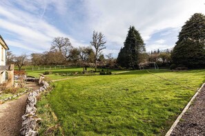 A grassy field with a stone wall, a tree, and a building in the background. - Lavish Farmhouse with Lake access, Gardens & Pool Table (Oakhill)