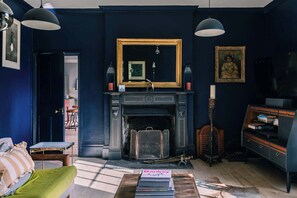 Une pièce avec une cheminée, un miroir, une bibliothèque et une table avec des livres.