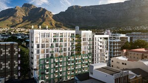Ein modernes Gebäude mit einem Fenstergitter, umgeben von anderen Bauten und einem Berg im Hintergrund.