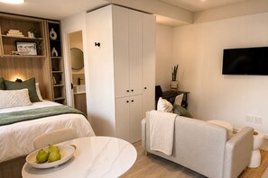 Ein modernes Schlafzimmer mit Bett, einer Sitzecke, einem Fernseher und einem Kleiderschrank.