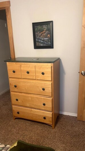A wooden dresser with drawers and knobs, a framed picture on the wall, and a carpeted floor. - Charming Family Escape with Porch, BBQ & Beach Access in McCall, Idaho (McCall)