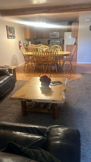 A living room with a leather sofa, a wooden coffee table with a vase, and a dining area with wooden chairs and a table. - Charming Family Escape with Porch, BBQ & Beach Access in McCall, Idaho (McCall)