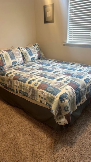 A bed with a quilt, a wall clock, and a window with blinds. - Charming Family Escape with Porch, BBQ & Beach Access in McCall, Idaho (McCall)
