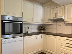 Uma cozinha com armários brancos, forno de aço inoxidável, pia e um vaso com flores na bancada.
