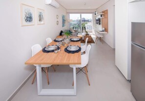A modern dining area with a wooden table, white chairs, and a city view through large windows. - Corporate Stays First Living - 401 (Asunción)