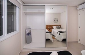 A bedroom with a sliding closet door, a bed with white bedding, a bedside table, and a wall-mounted air conditioner. - Corporate Stays First Living - 401 (Asunción)