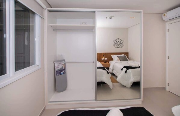 A bedroom with a sliding closet door, a bed with white bedding, a bedside table, and a wall-mounted air conditioner. - Corporate Stays First Living - 401 (Asunción)