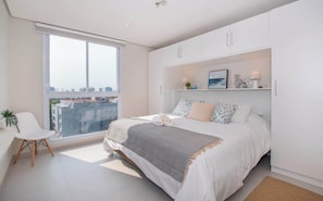 A bedroom with a large window, a bed, a chair, and a white wardrobe. - Corporate Stays First Living - 401 (Asunción)