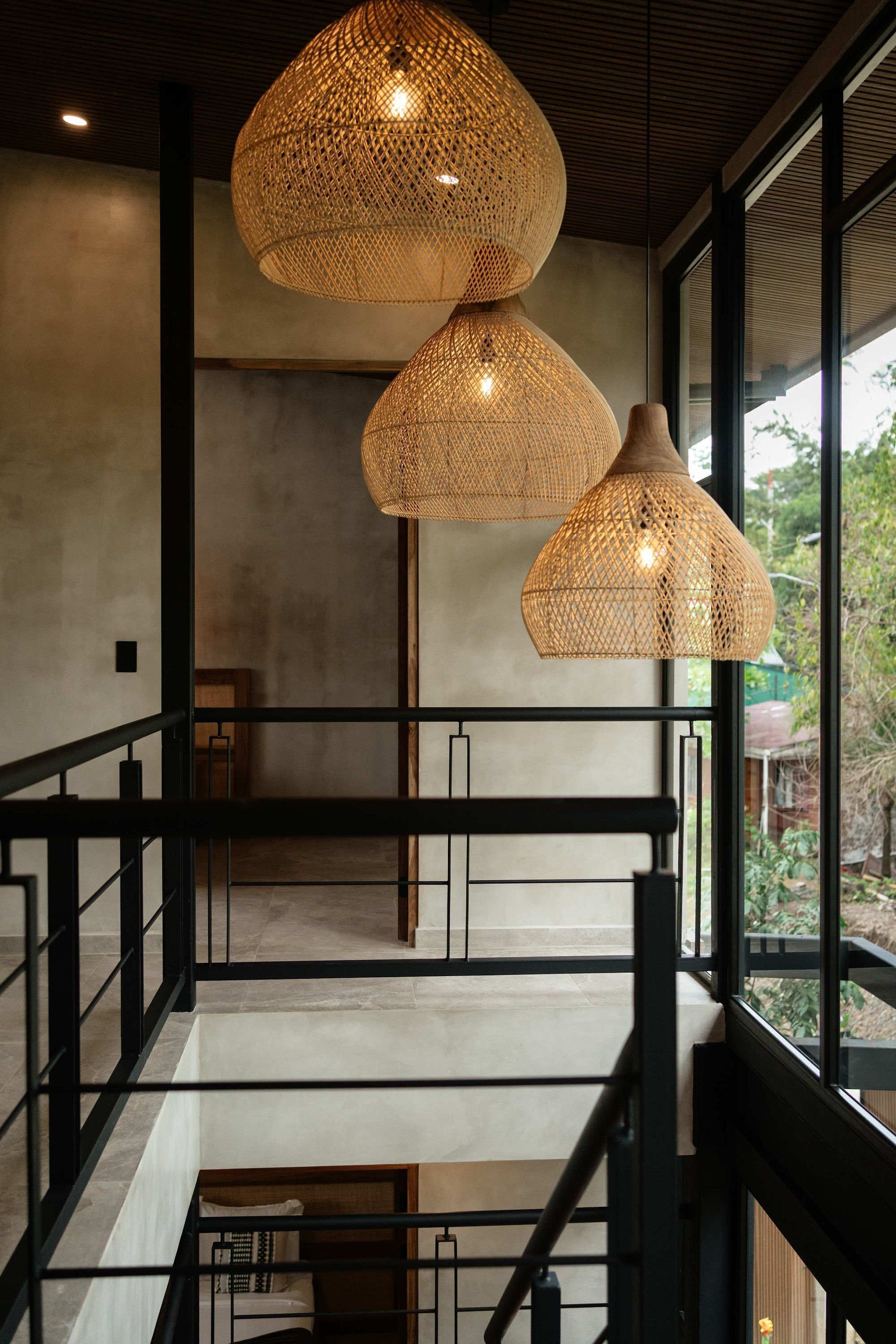 A modern interior with a staircase, large windows, and three woven pendant lights.