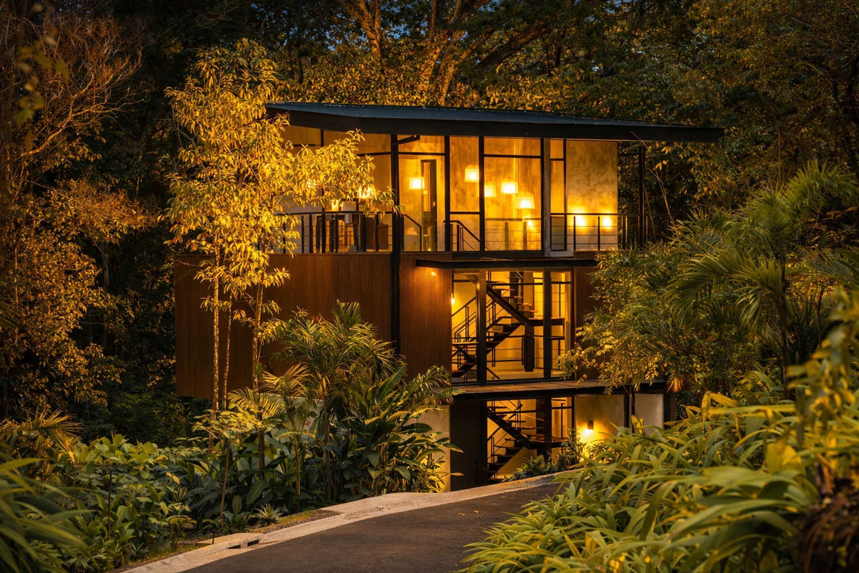 A modern, multi-level wooden structure surrounded by dense foliage, with a staircase leading to an upper level.