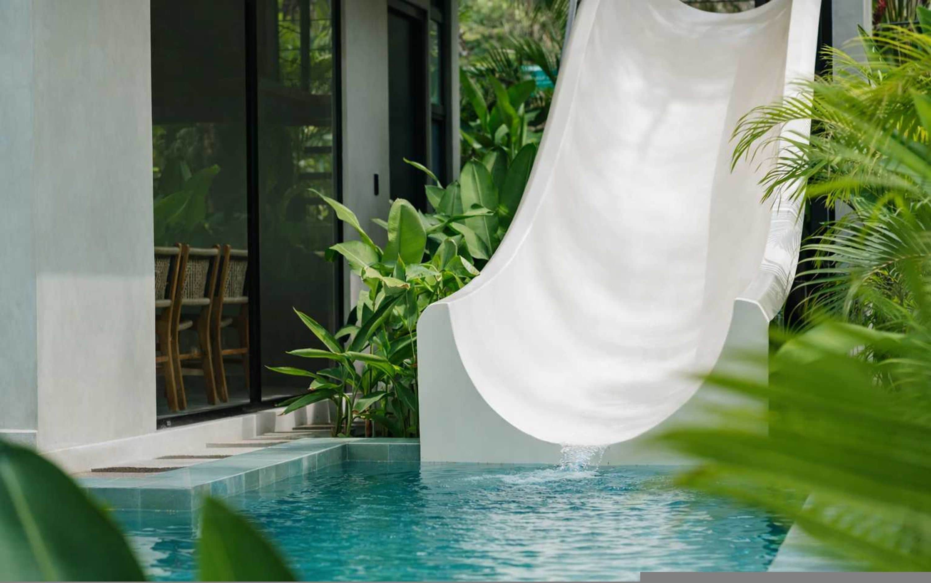 A pool with a white slide, surrounded by greenery.