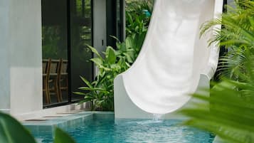A pool with a white slide, surrounded by greenery.