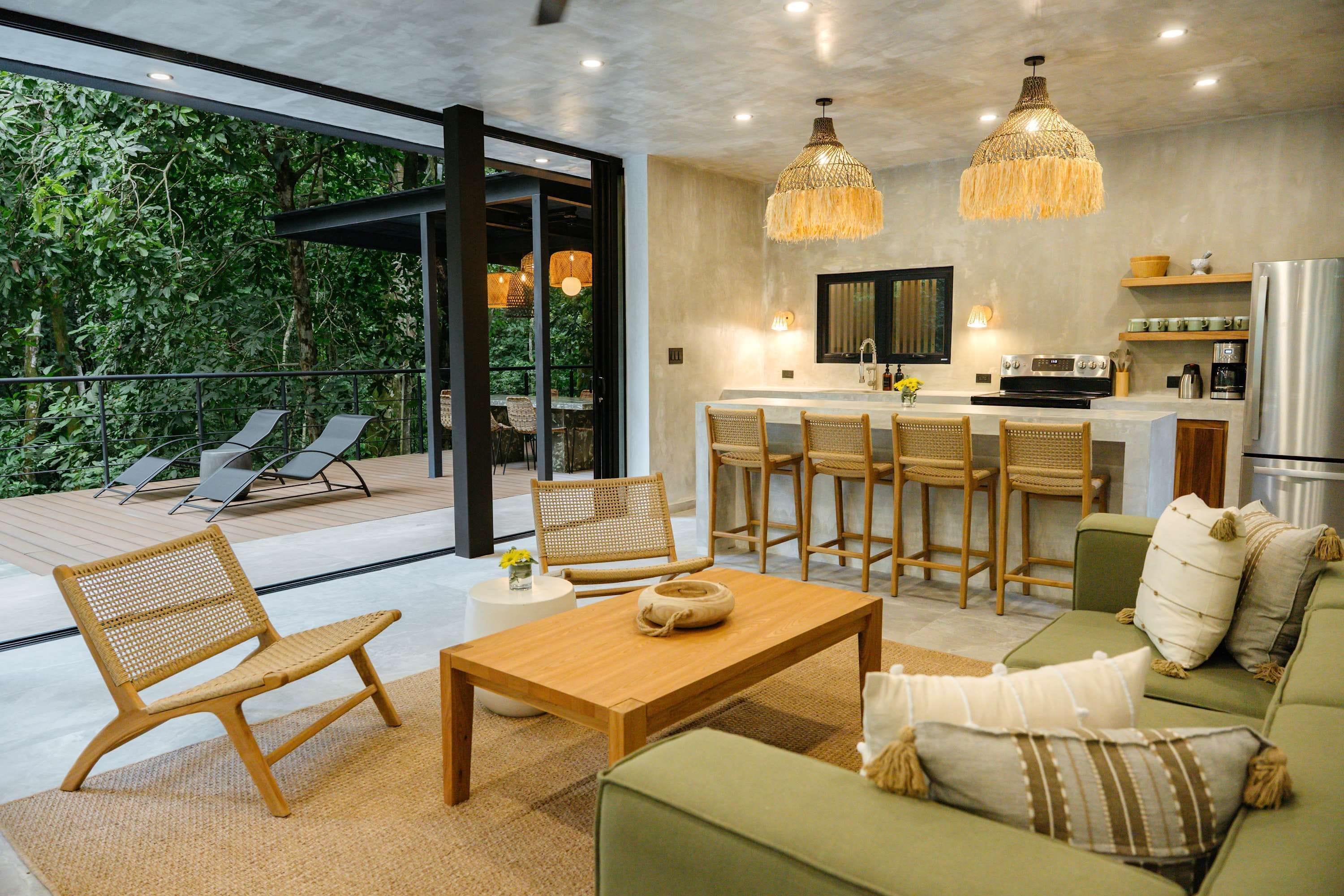 A modern kitchen with a bar area, a dining set, and a seating area with a view of greenery.