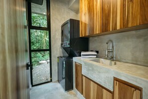 A compact kitchen with a built-in washer, a sink, and wooden cabinets. - New Private 3BR Luxury Tree House With Slide (Quepos)