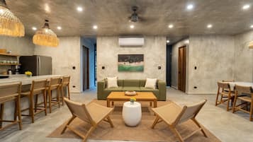 Uma sala ampla com sofá, mesa de centro e cadeiras, cozinha com banquetas e área de jantar com mesa e cadeiras.