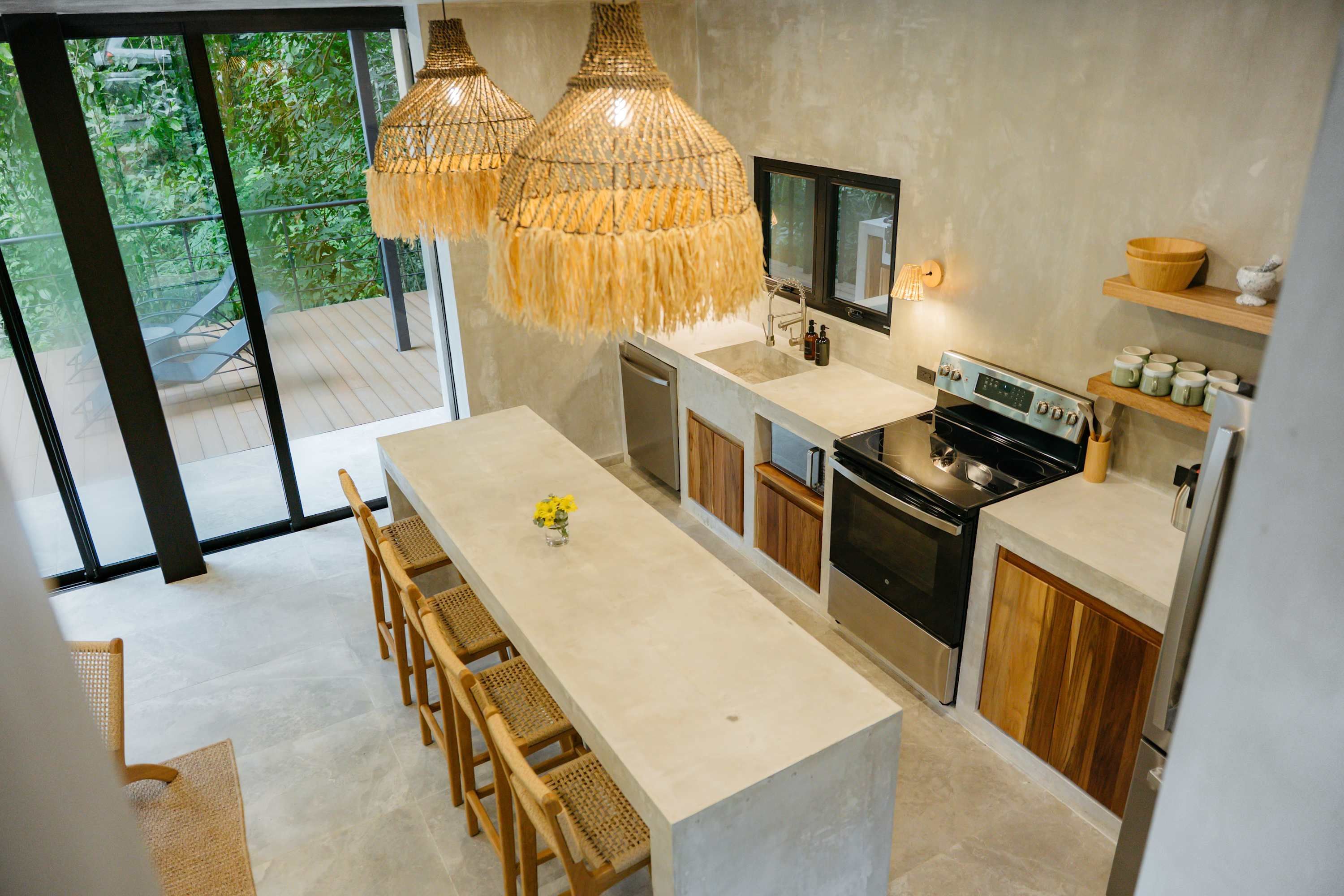 A modern kitchen with a central island, wooden cabinets, and a large window overlooking greenery.