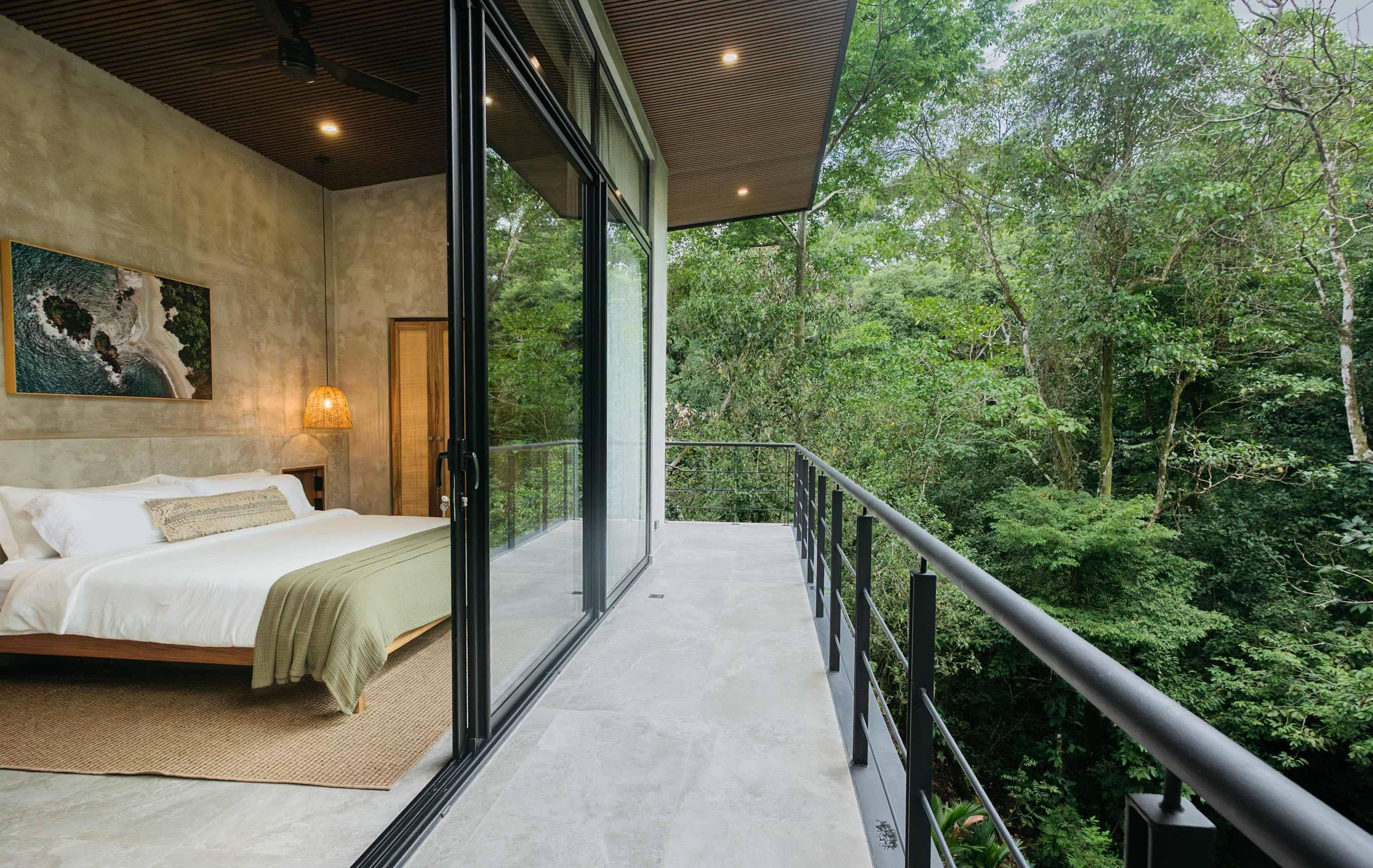A bedroom with a large bed, a view of the forest, and a balcony with a railing.