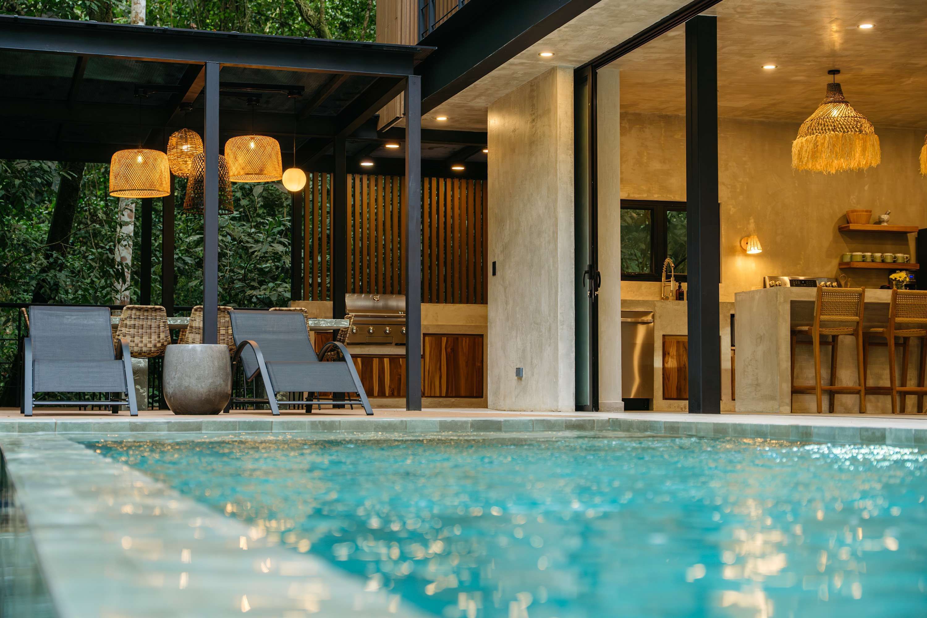 A modern outdoor pool area with lounge chairs and a barbecue grill.