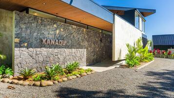 A modern building with a stone facade, a wooden slatted roof, and a gravel pathway with plants.