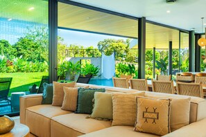 Un salon moderne doté d’un grand canapé, de nombreux coussins et offrant une vue sur une piscine et un jardin.