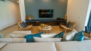 Ein modernes Wohnzimmer mit Flachbildfernseher an der Wand, einem runden Couchtisch und zwei Korbstühlen.