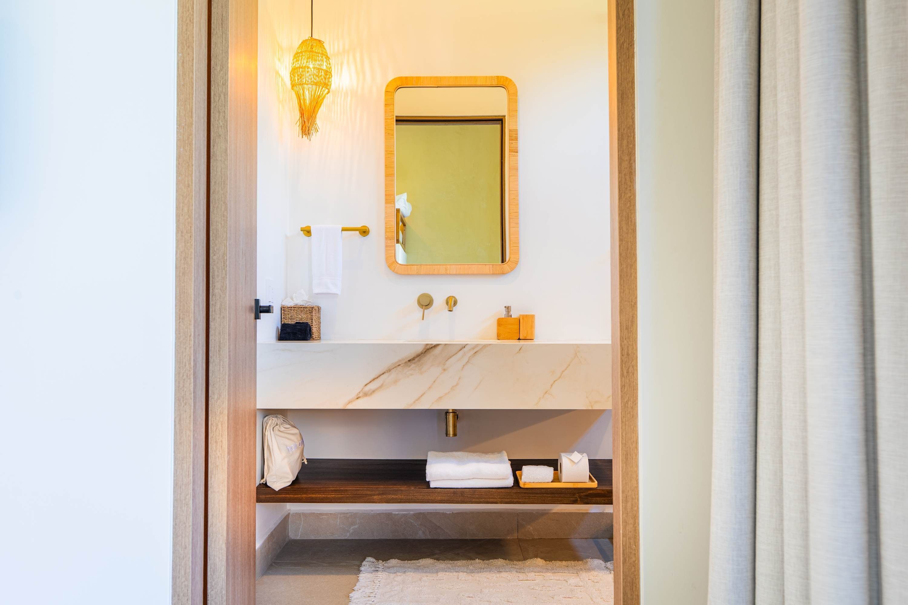 A bathroom with a marble vanity, a wooden shelf, a towel rack, and a mirror with a gold frame.