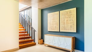 Eine Treppe mit hölzernen Stufen und Metallgeländern, ein weißer Schrank mit strukturierter Oberfläche und zwei gerahmte Kunstwerke an einer blauen Wand.