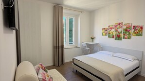 A bedroom with a bed, a desk, a chair, a TV, and a window with curtains. - LINDA affittacamere (ANCONA)