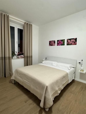 Een slaapkamer met een bed, gordijnen, een nachtkastje en decoratie aan de muur.