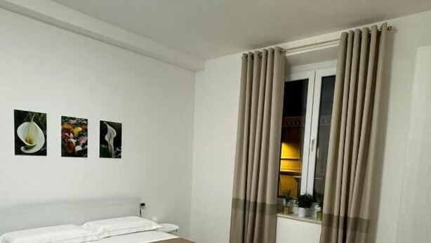 A hotel room with a bed, a desk, and a window with curtains. - LINDA affittacamere (ANCONA)