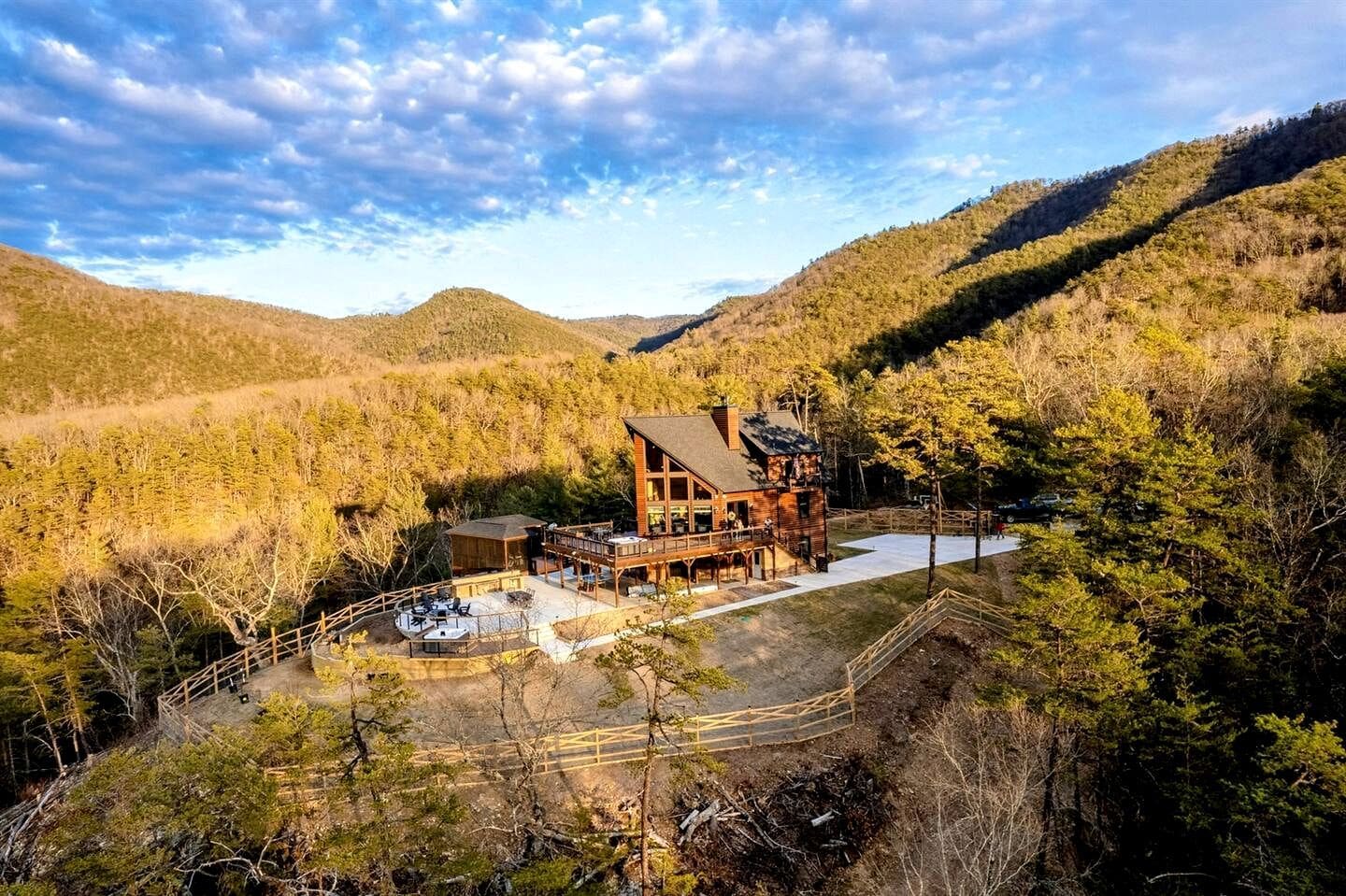 A lodge with a deck and outdoor seating area, surrounded by forested hills.