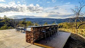 Eine Terrasse im Freien mit einer Steibar und Sitzgelegenheiten, mit Blick auf eine Berglandschaft.