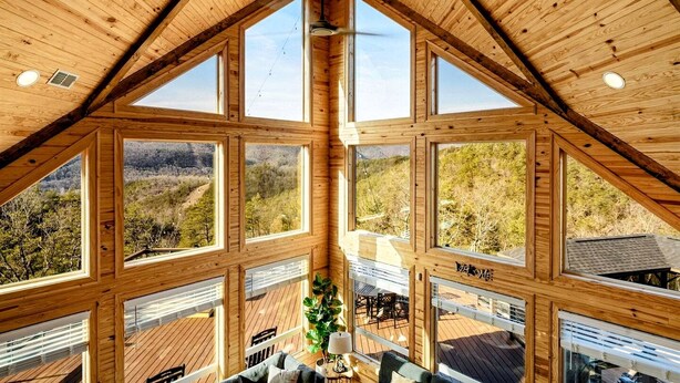 Ein Zimmer mit hohen Decken und großen Fenstern, das einen Blick auf eine bewaldete Landschaft bietet.