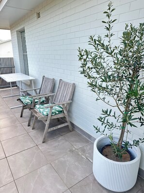 Eine Terrasse mit zwei Holzstühlen und einem Tisch, einer Topfpflanze und einer weißen Backsteinmauer.