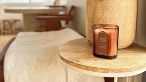 Um quarto com uma cama, uma mesa redonda de madeira com uma vela e um grande cachepot de madeira.