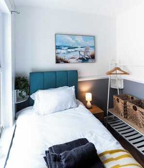 Ein ordentlich bezogenes Bett mit Kopfteil, einer Nachttischlampe, einem Wandbild und einem Regal mit Körben.