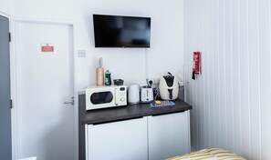Eine Küchenzeile mit Mikrowelle, Toaster und Kaffeemaschine, einem darüber montierten Fernseher sowie einer Wanddecke.