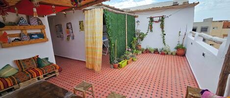 A rooftop terrace with a checkered floor, a sofa, a table, and potted plants.