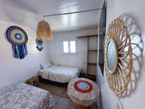 A bedroom with two beds, a small stool, a hanging light, and decorative wall art.