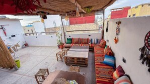 A rooftop terrace with a wooden table, a sofa with colorful cushions, and a wall with dreamcatchers. - Jurassic Surf House Anza (Agadir)