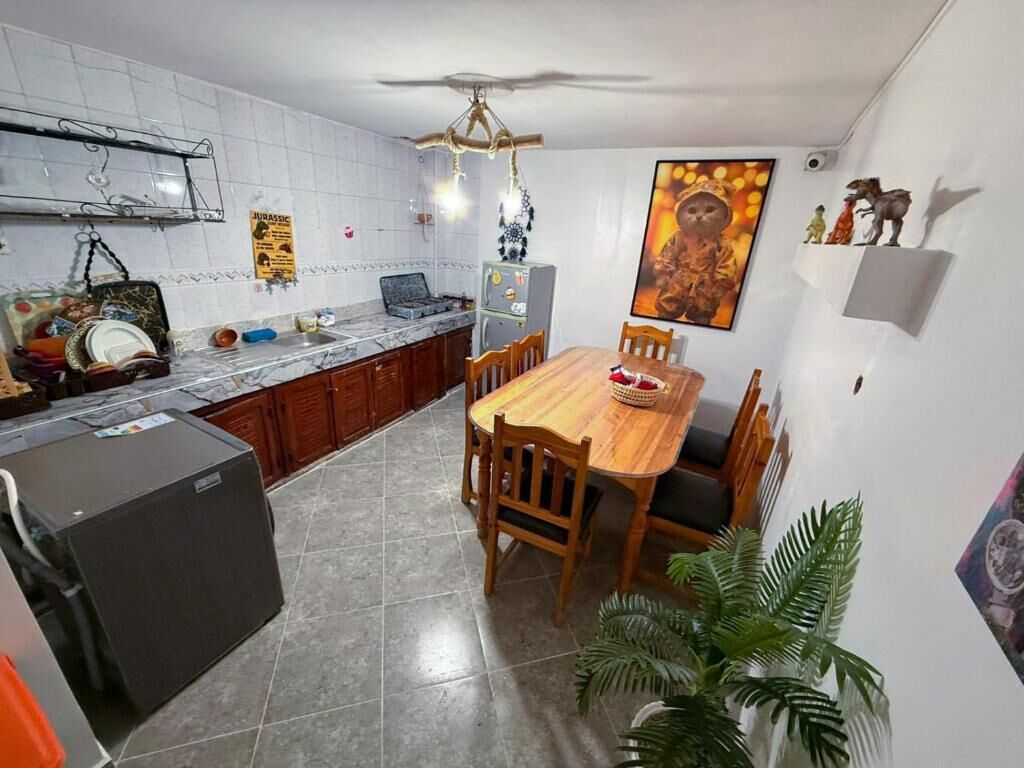 Une cuisine équipée d’une table à manger, de chaises, d’un réfrigérateur et d’un ventilateur de plafond.