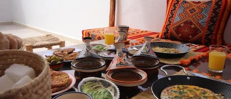 Una mesa de comedor con platos tradicionales marroquíes, una cesta tejida y un vaso de jugo de naranja.