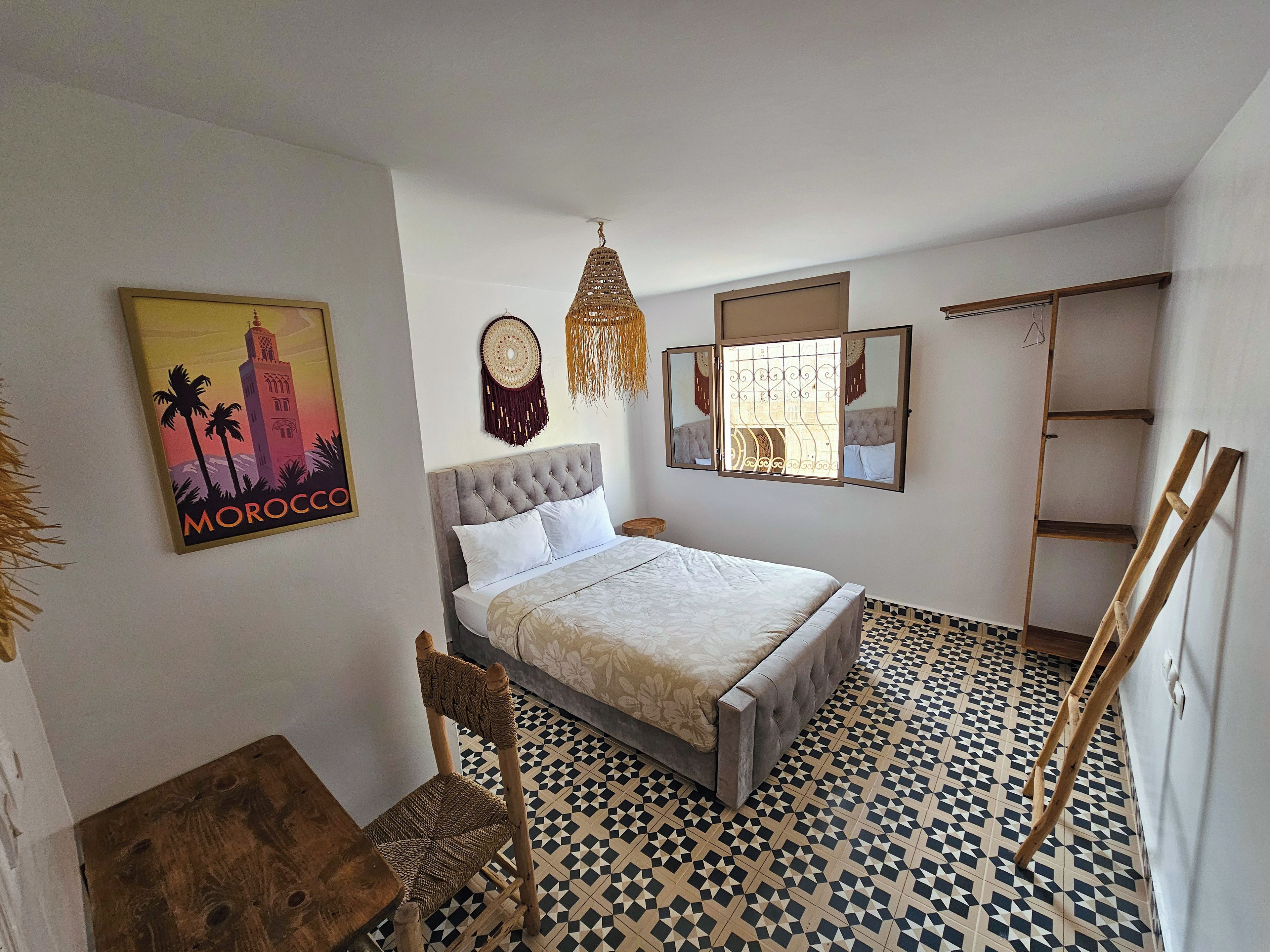 A bedroom with a bed, a chair, a wall-mounted mirror, a decorative wall hanging, and a framed picture.