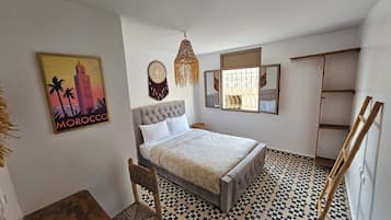 Een slaapkamer met een bed, een stoel, een spiegel aan de muur, een decoratieve wandversiering en een ingelijst kunstwerk.