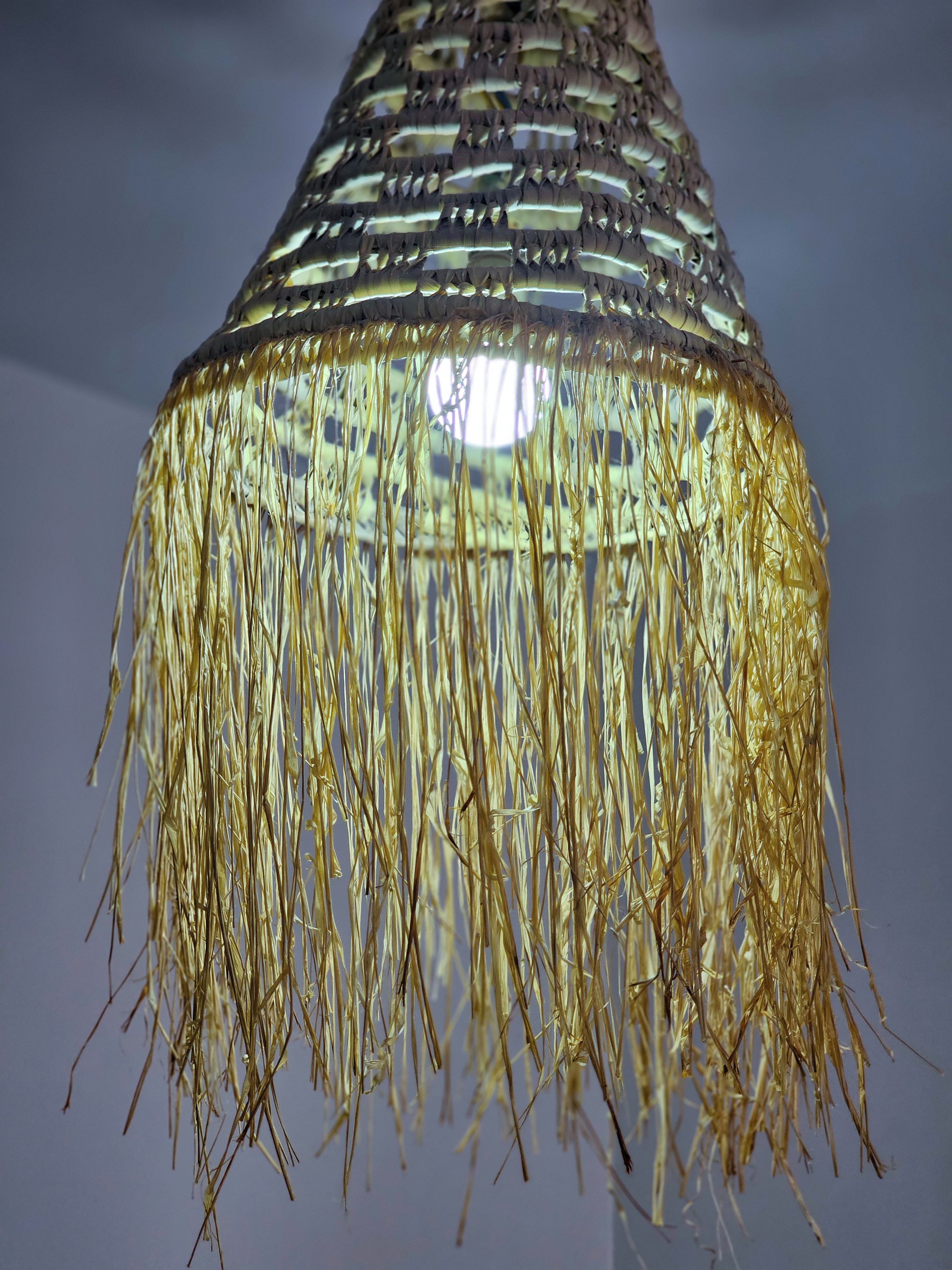 A hanging light fixture with a woven pattern and tassels.