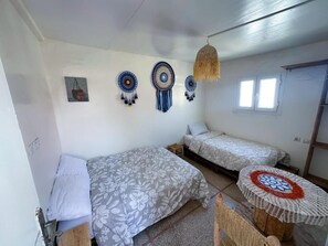 A room with two single beds, a small table with a crocheted tablecloth, and wall decorations including dream catchers and a framed picture. - Jurassic Surf House Anza (Agadir)