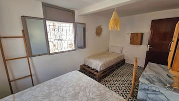A room with a bed, a window with bars, a hanging light fixture, and a door.