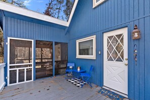 Un bâtiment bleu avec un porche couvert, une porte blanche et une fenêtre ornée d’un motif en losange.